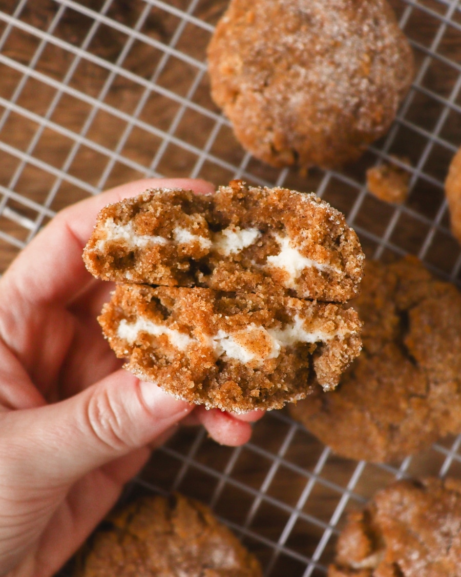 Close-up photo the inside of the Keto Gingerbread Cheesecake Cookie with other cookies in the background. The cookie is opened to reveal the tempting cheesecake cream cheese filling.