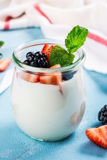 greek yogurt with berries in a small glass jar on blue background