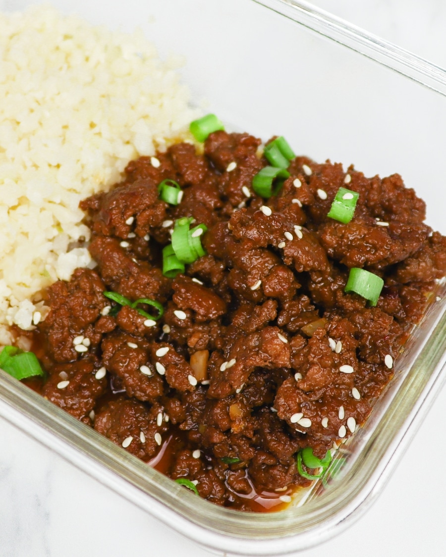 Keto Korean Beef with sliced green onions, sesame seeds, and riced cauliflower in a meal prep glass container side shot