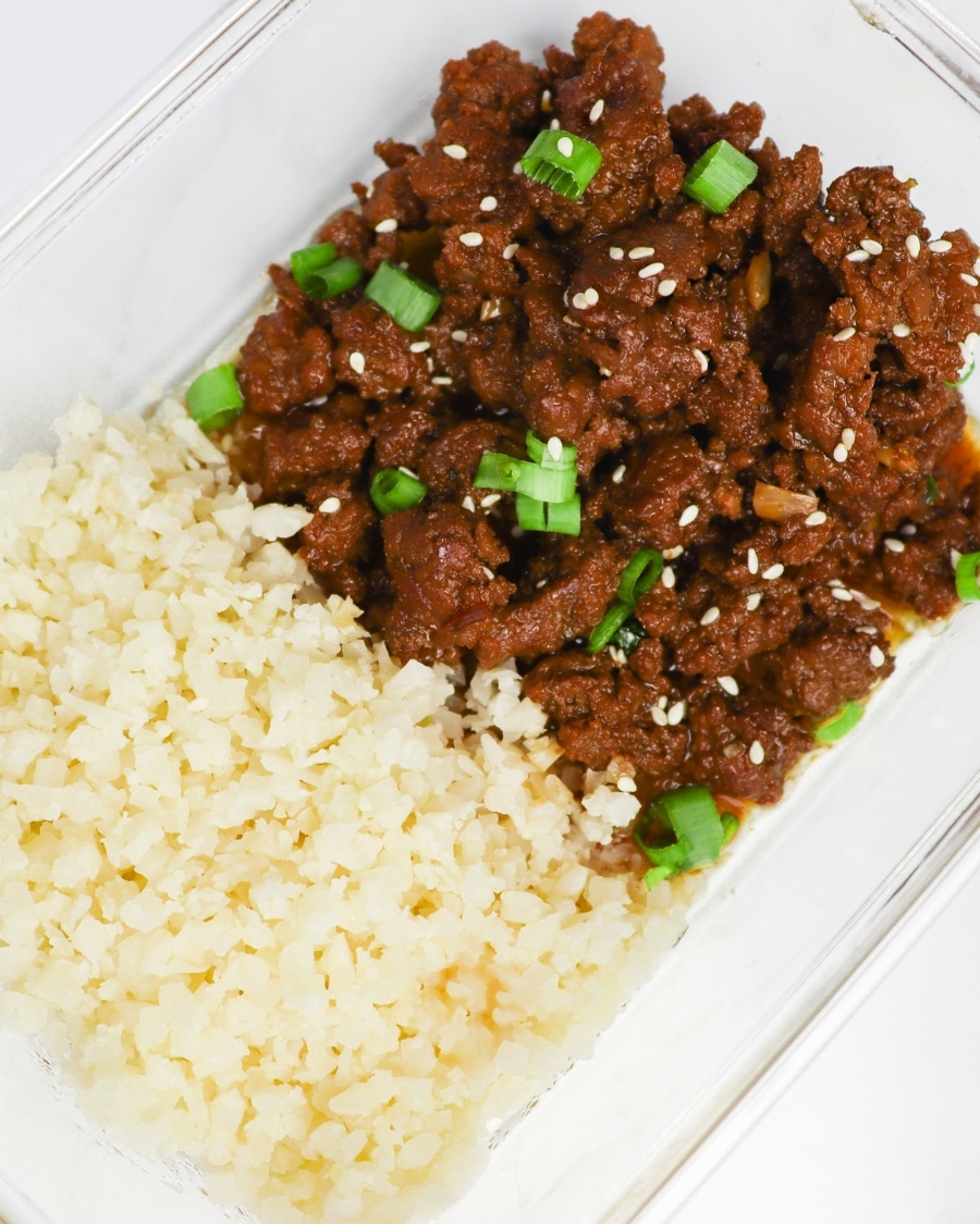 Keto Korean Beef with sliced green onions, sesame seeds, and riced cauliflower in a meal prep glass container overhead shot