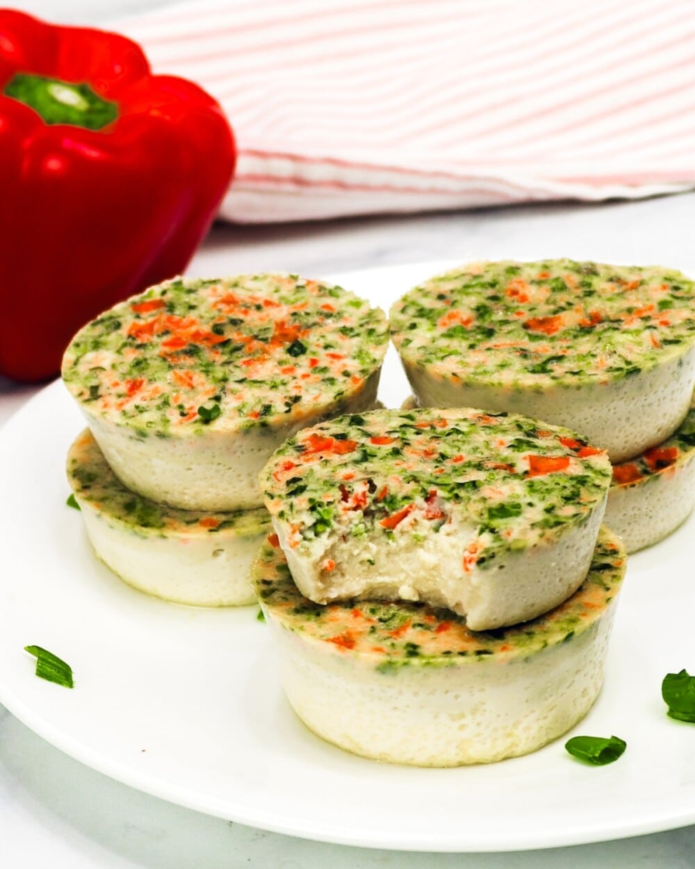 keto egg bites on a white plate with a bell pepper in the background, one bite taken out of one egg bite