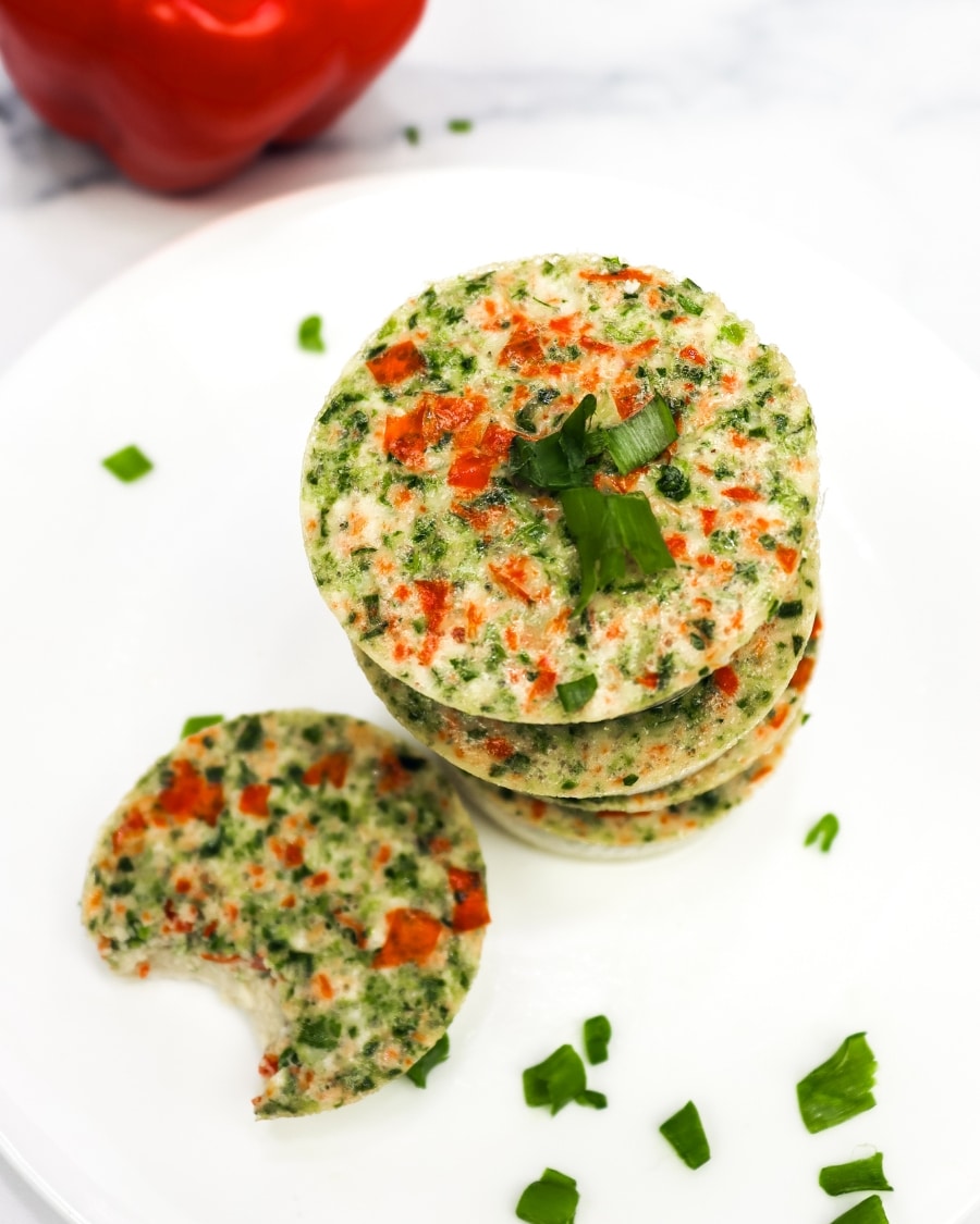 keto egg bites on a white plate with a bell pepper in the background, one bite taken out of one egg bite