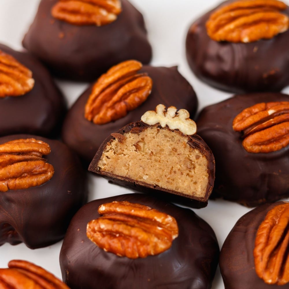 keto pecan pie truffles mounded together, dark chocolate shell shaped like oblong with a single pecan on top, single one showing cross section in the middle