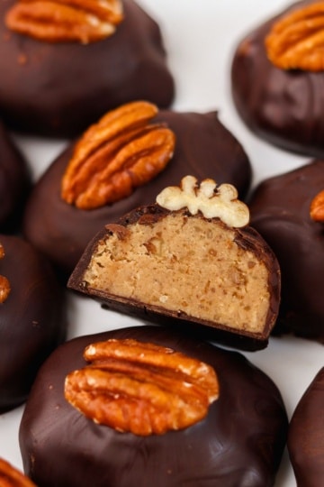 keto pecan pie truffles mounded together, dark chocolate shell shaped like oblong with a single pecan on top, single one showing cross section in the middle