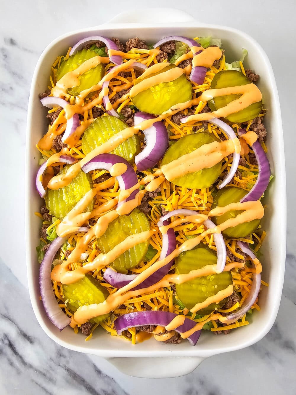 chopped lettuce and ground beef and shredded cheese and pickles and onions and thousand island dressing in a casserole dish