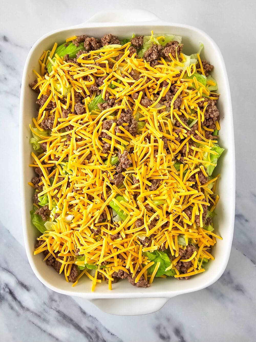 chopped lettuce and ground beef and shredded cheese in a casserole dish