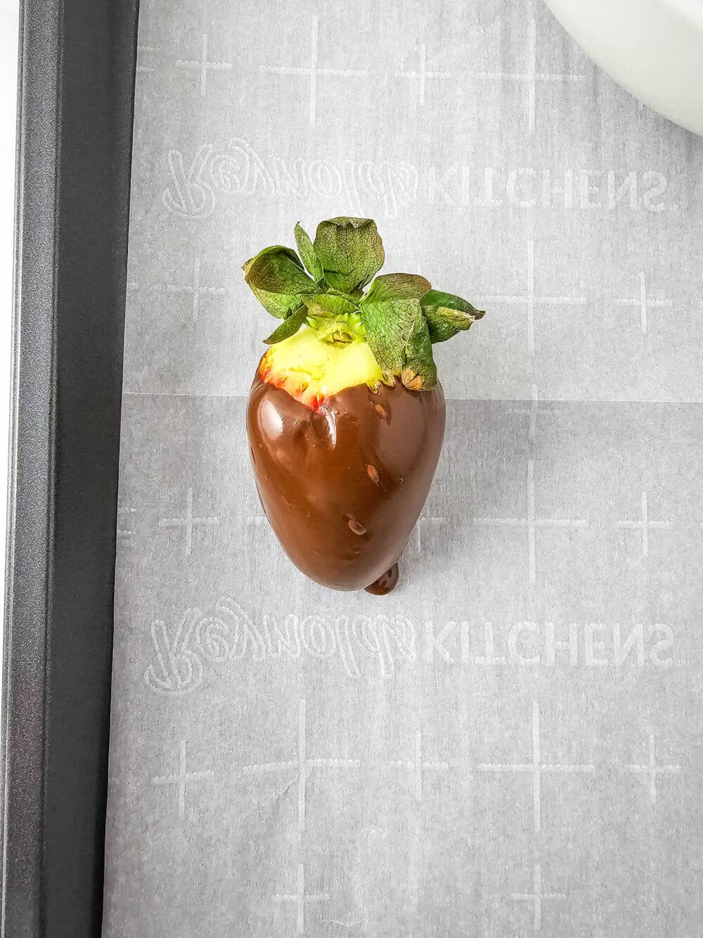 one strawberry covered in sugar free melted chocolate on parchment paper
