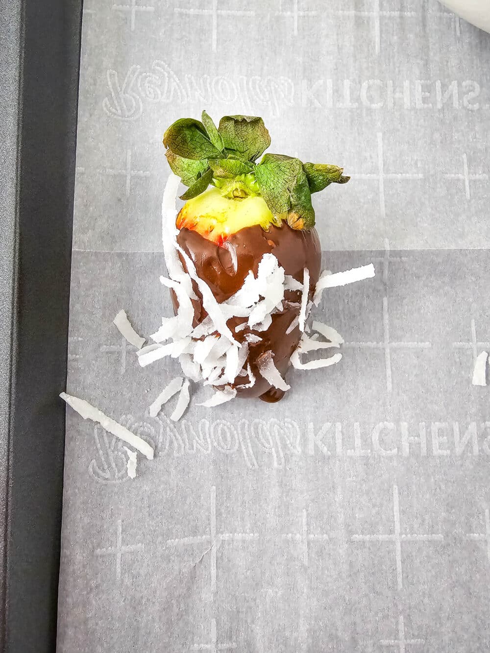 one strawberry covered in sugar free melted chocolate and unsweetened coconut flakes on parchment paper