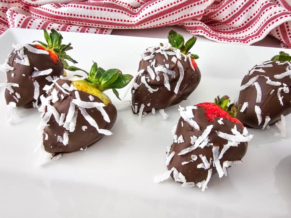 5 strawberries covered in sugar free melted chocolate and unsweetened coconut on plate