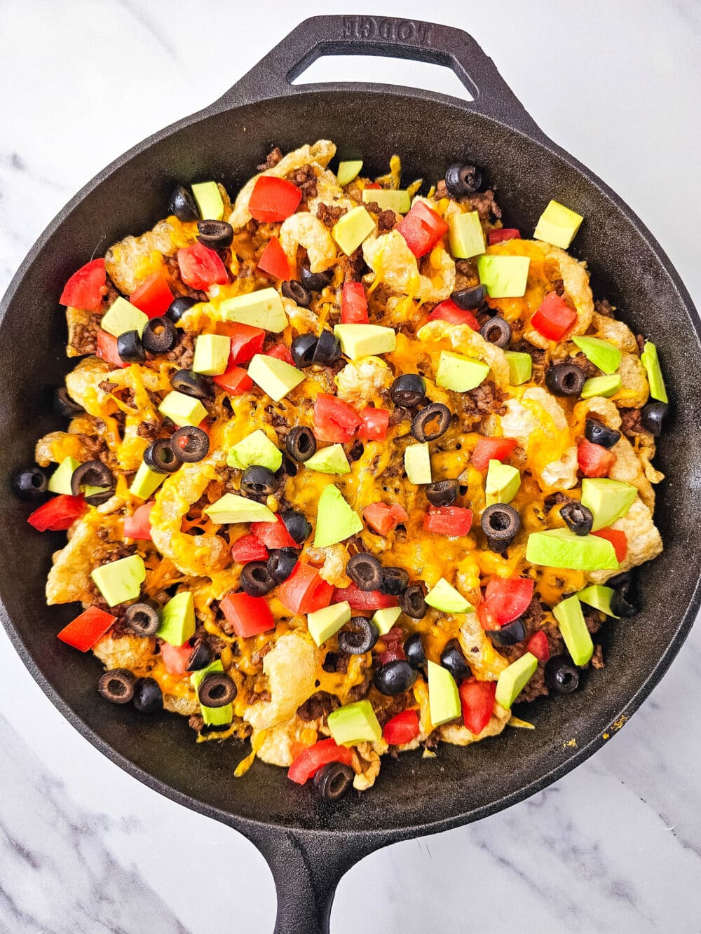 pork rinds and ground beef and cheese and tomatoes and avocados and olives in iron skillet