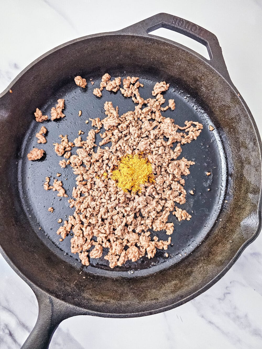 browned ground beef in iron skillet with taco seasoning
