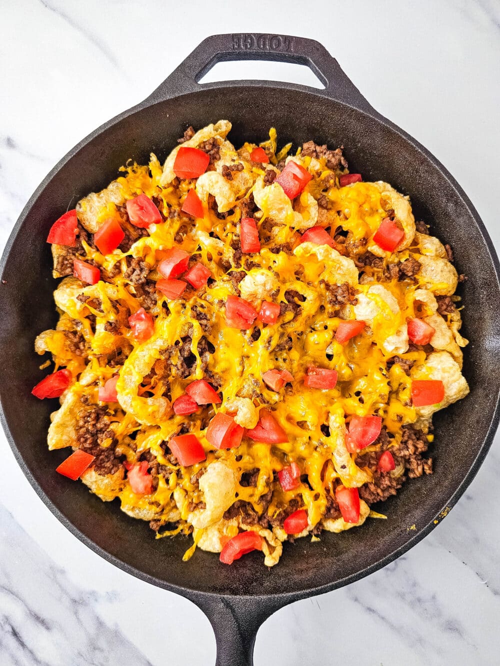 pork rinds and ground beef and cheese and tomatoes in iron skillet