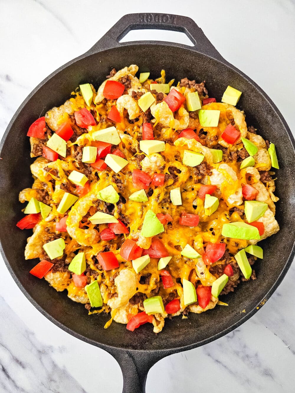 pork rinds and ground beef and cheese and tomatoes and avocados in iron skillet