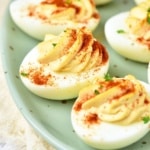 close up of deviled eggs sprinkled with paprika on green platter