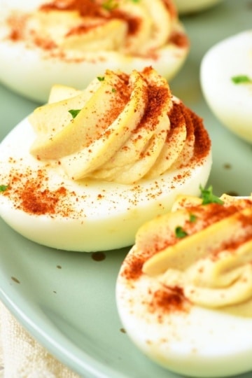 close up of deviled eggs sprinkled with paprika on green platter