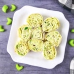 sliced chicken avocado pinwheels on a white platter with blue background and celery scattered