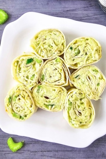 sliced chicken avocado pinwheels on a white platter with blue background and celery scattered