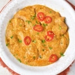 Butter Chicken with sliced red peppers on top in white bowl with red napkin underneath
