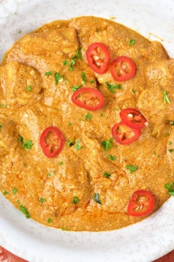 Butter Chicken with sliced red peppers on top in white bowl with red napkin underneath