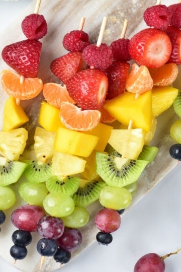 Rainbow Fruit Skewers on a marble cutting board overhead view with grapes nearby