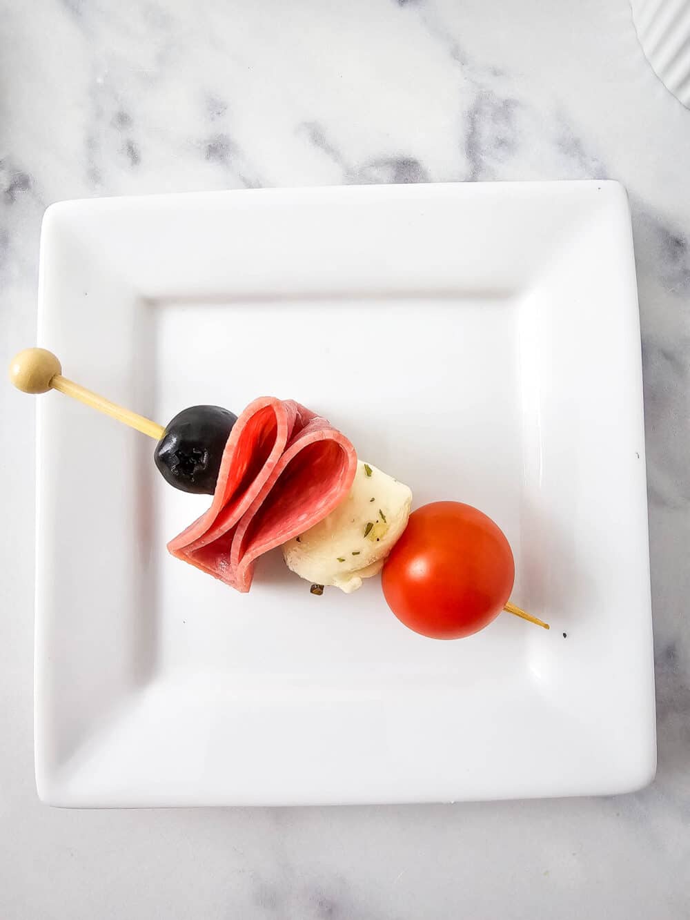 olive, salami, mozzarella ball, and cherry tomato on a skewer