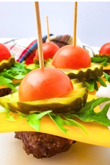 side view of Keto Mini Cheeseburger Bites stacked with tomato, pickle, cheese, lettuce, and a mini burger