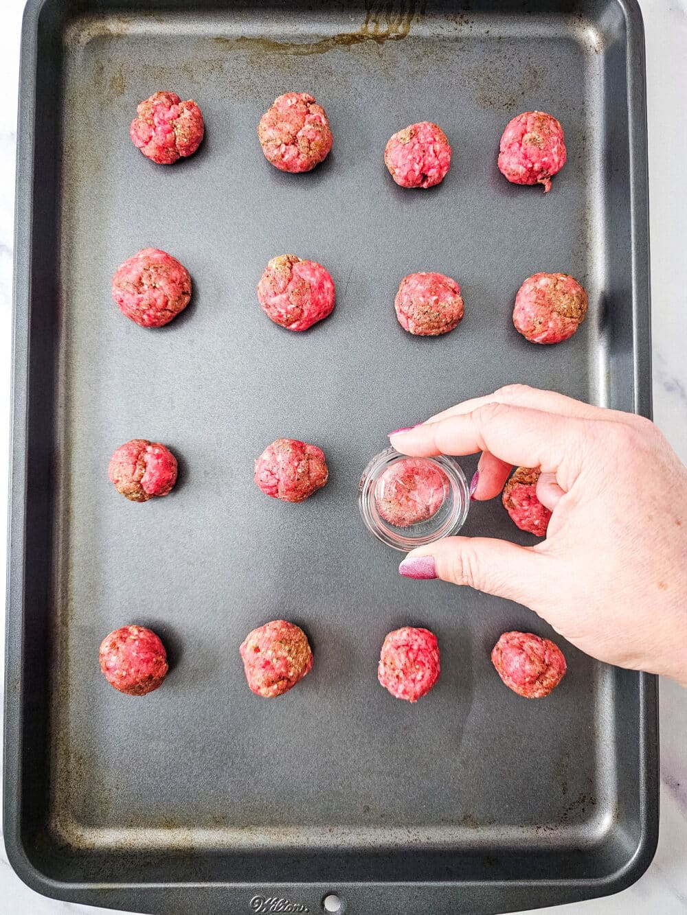 smashing ground beef balls on a sheet pan