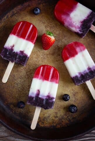 3 popsicles on a pan with strawberry nearby