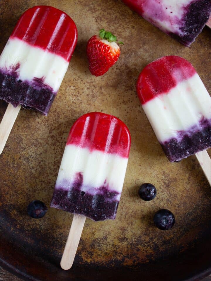 3 popsicles on a pan with strawberry nearby