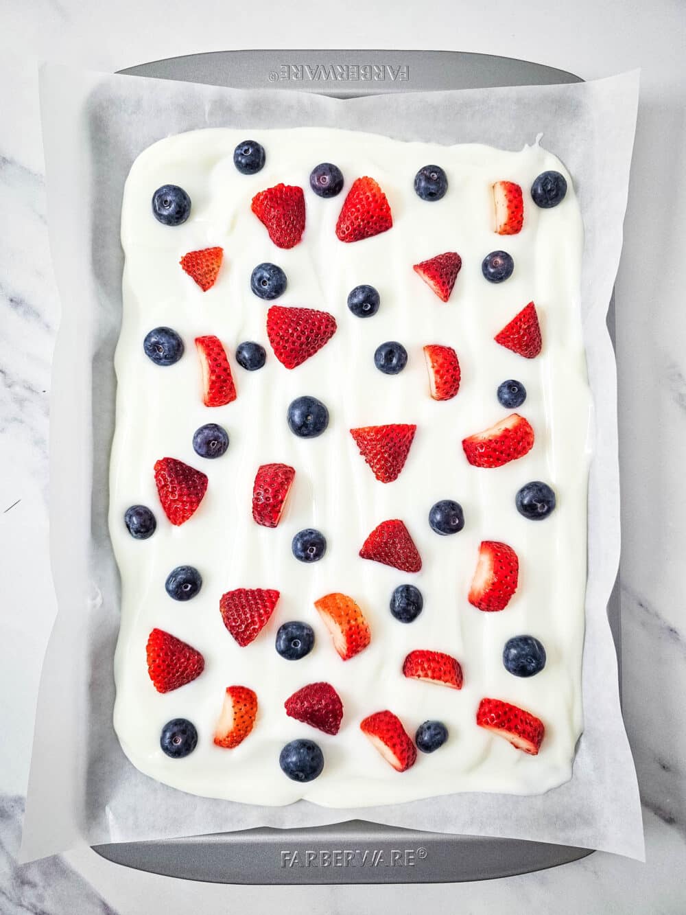 strawberries and blueberries on greek yogurt on a baking pan