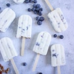 scattered Keto Protein Blueberry Cheesecake Popsicles with blueberries and pecans nearby on blue background