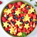 fruit salad with pineapple cut into stars, strawberries, and blueberries in a green bowl