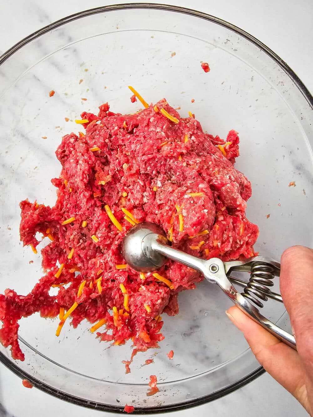 scooping meat mixture out of a mixing bowl with a cookie scoop