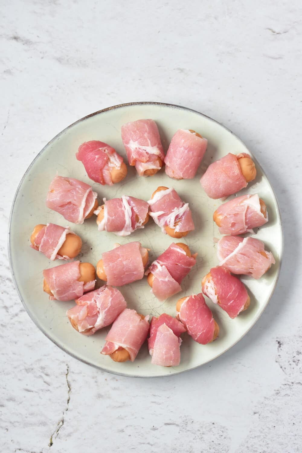 pigs in a blanket ready for oven on round plate, overhead view