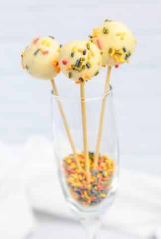 3 cake pops in a wine glass with sprinkles on the bottom
