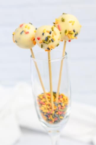 3 cake pops in a wine glass with sprinkles on the bottom