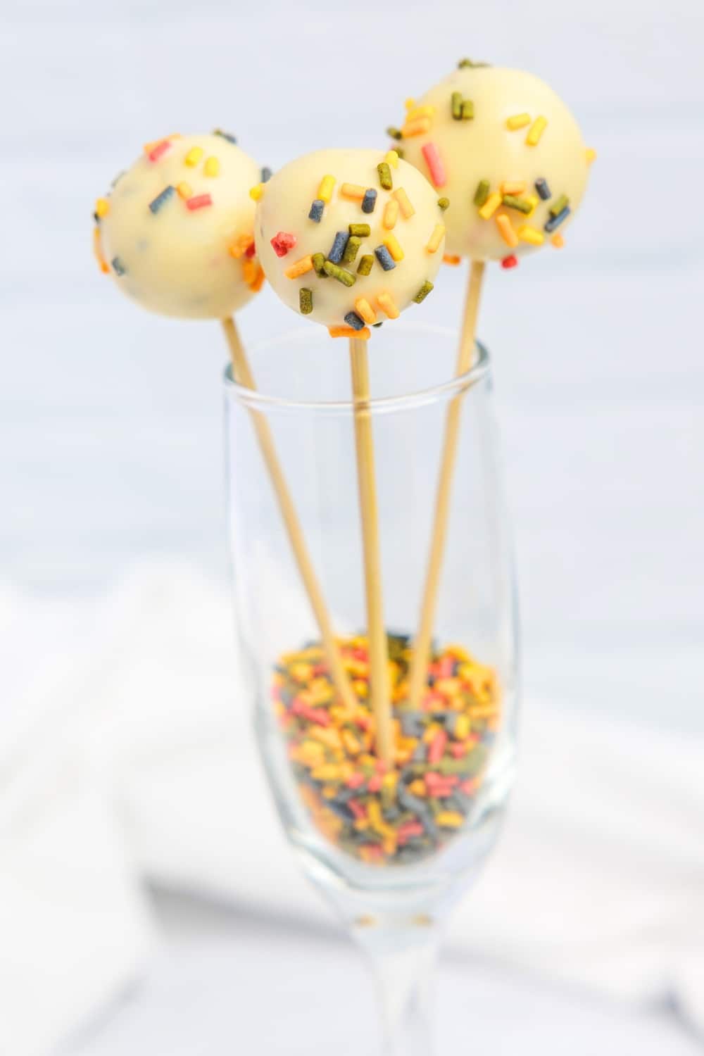3 cake pops in a wine glass with sprinkles on the bottom