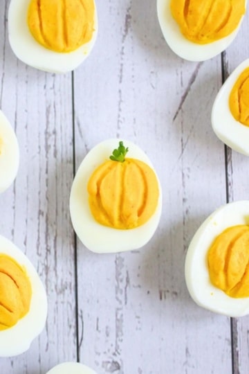 pumpkin deviled eggs on a white wood background
