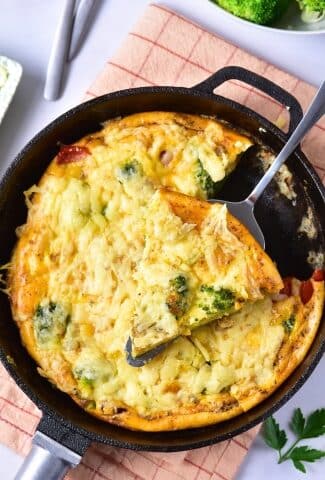 Baked broccoli cheese frittata in a skillet with a slice being lifted out.
