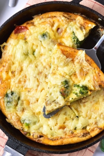 Baked broccoli cheese frittata in a skillet with a slice being lifted out.