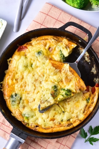Baked broccoli cheese frittata in a skillet with a slice being lifted out.