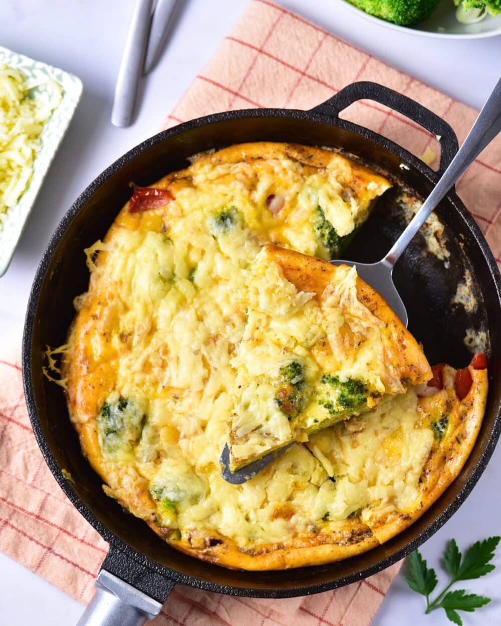 Golden broccoli cheese frittata in a skillet with a serving spoon.