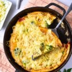 Golden broccoli cheese frittata in a skillet with a serving spoon.
