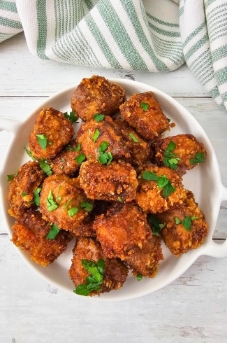 Plate of golden brown fried steak nuggets garnished with chopped parsley.