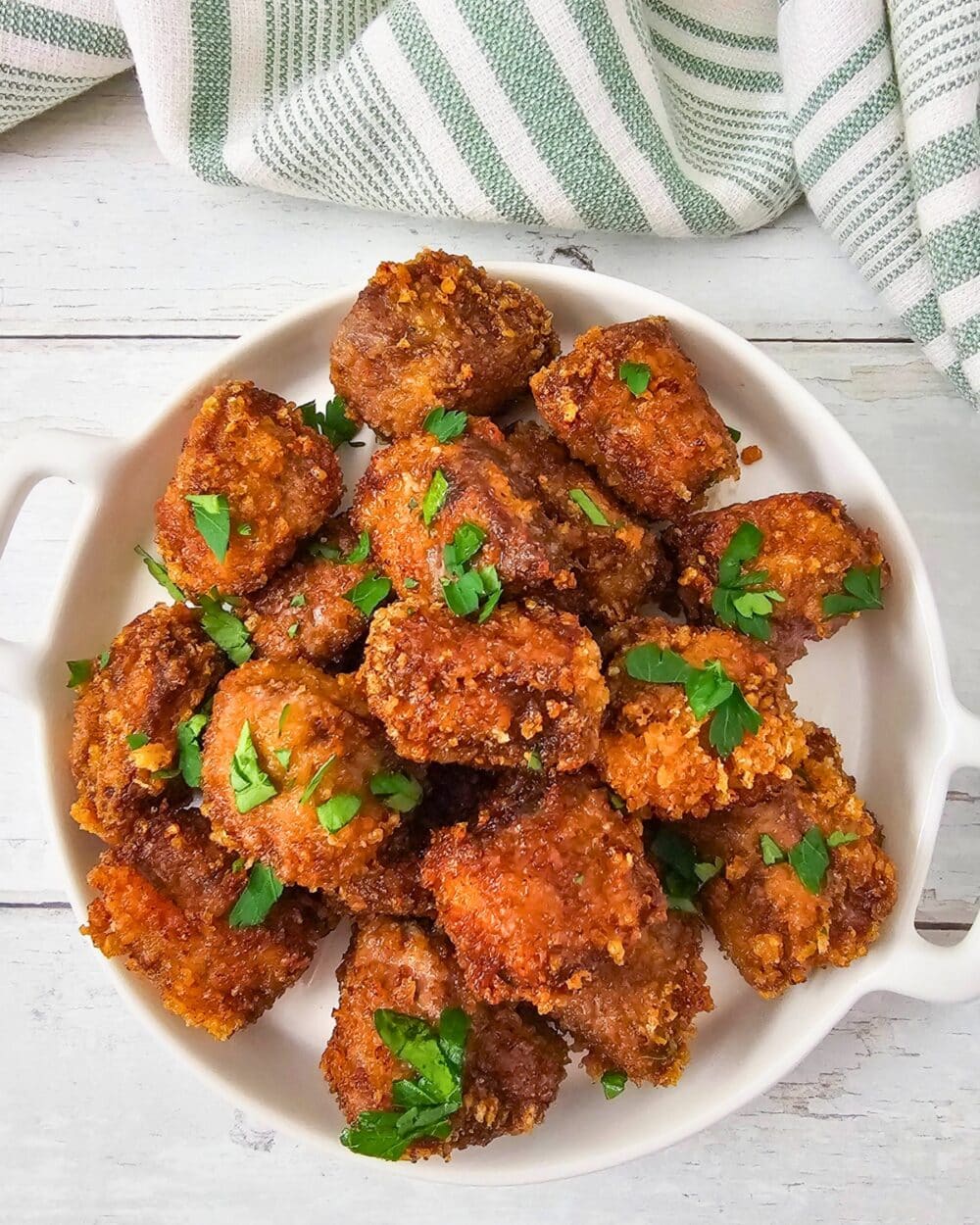 Close-up of crispy steak nuggets piled on a white plate with parsley garnish.