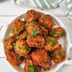 Close-up of crispy steak nuggets piled on a white plate with parsley garnish.