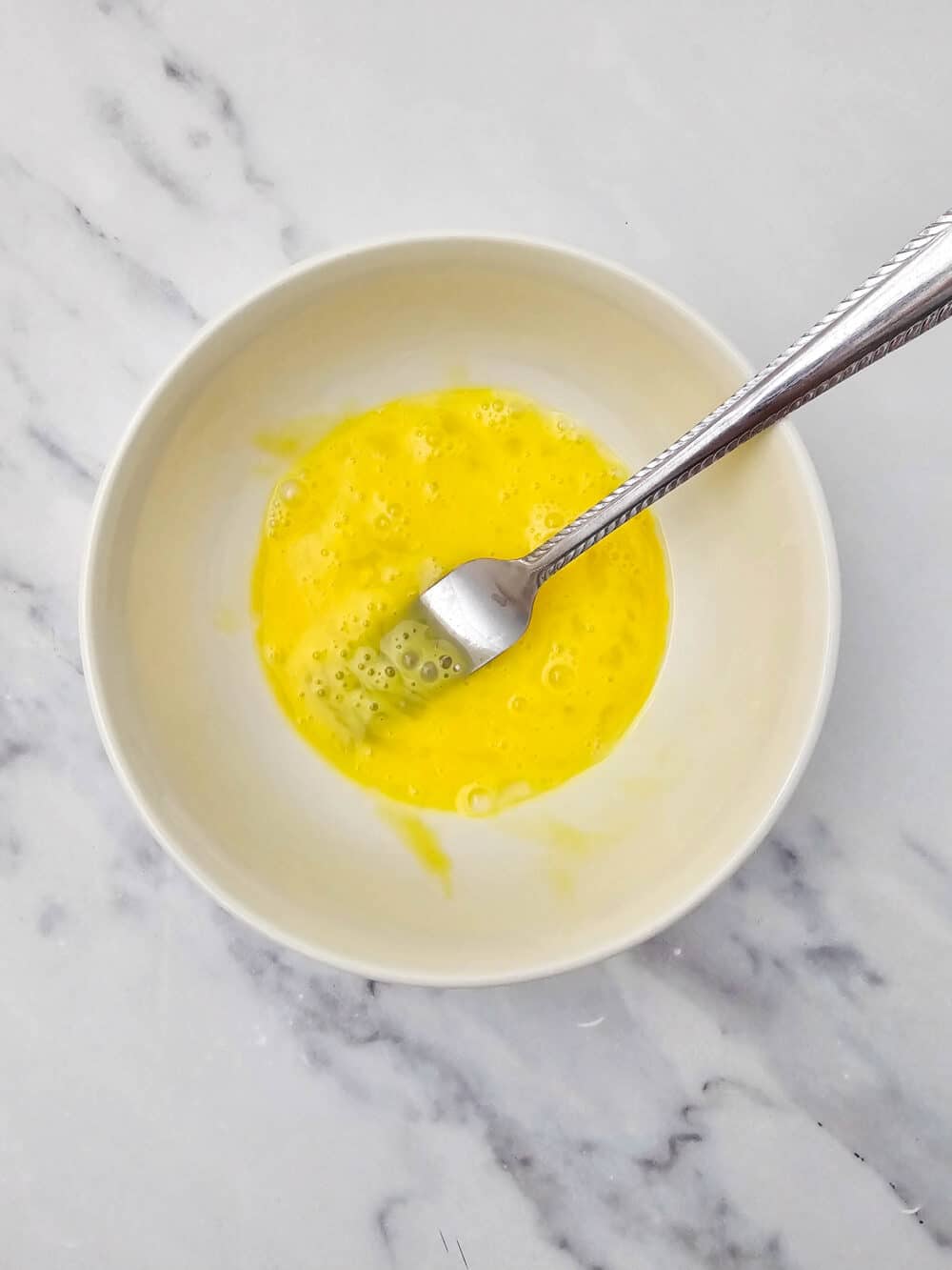 Bowl of a beaten egg mixture with fork resting inside.