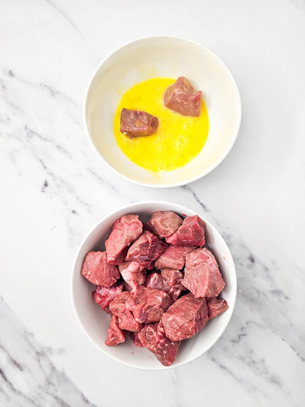 Bowl of raw steak chunks dipped into a beaten egg mixture.