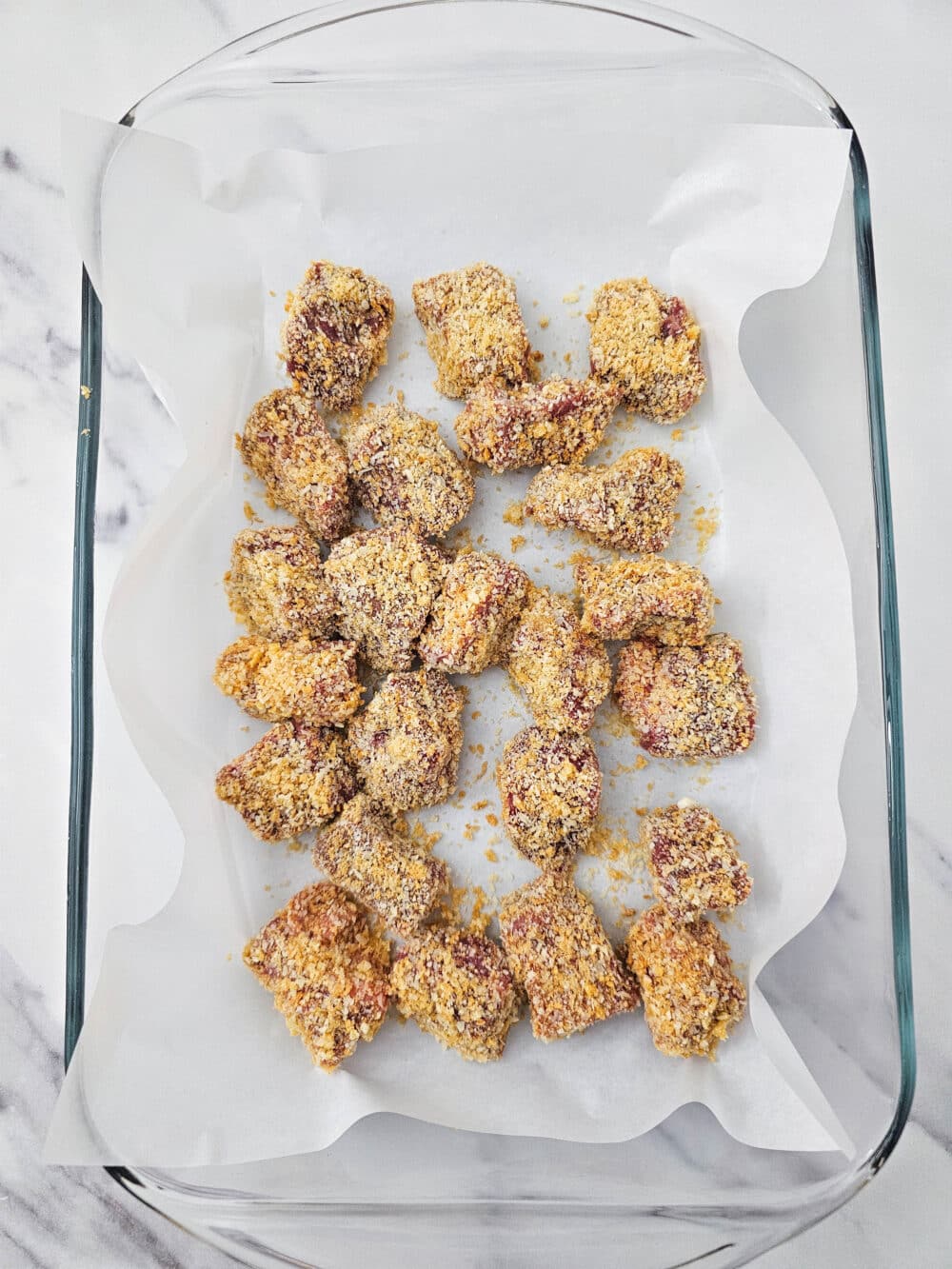 Breaded steak chunks arranged on a parchment-lined baking dish, ready to freeze.