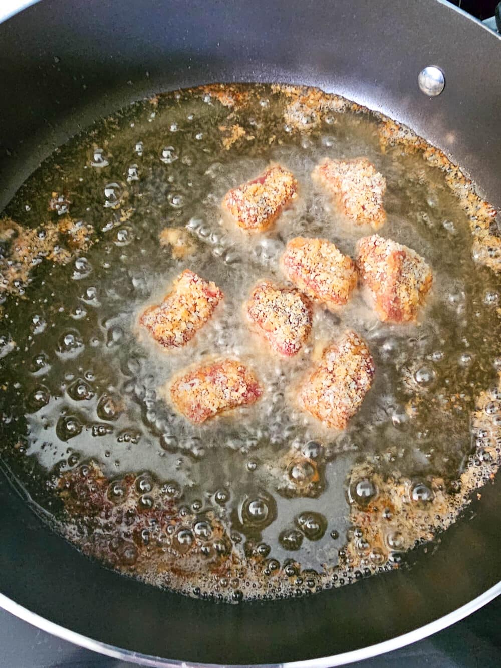 Breaded steak nuggets frying in hot oil inside a skillet.